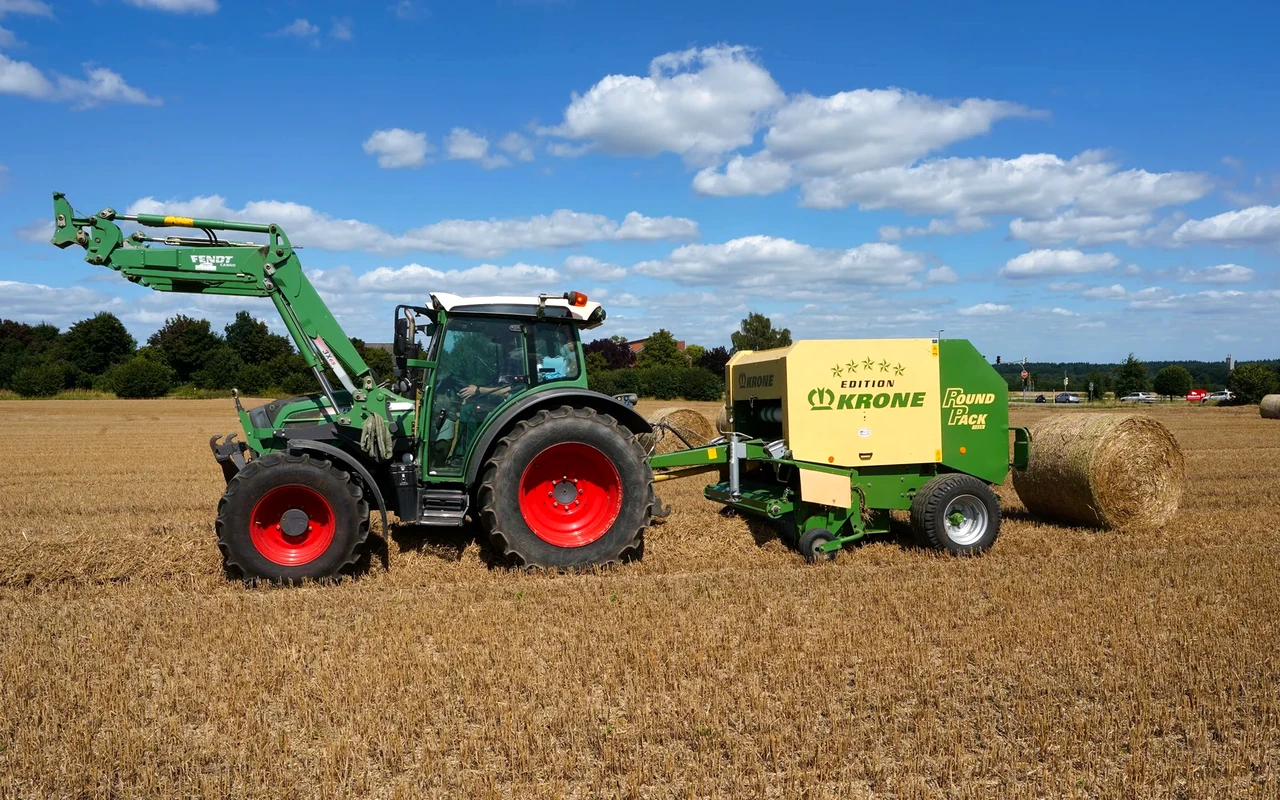 Traktor mit Rundballenpresse auf einem abgeernteten Feld